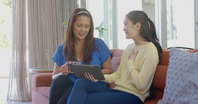 Sitting on couch, asian mother and daughter using tablet and smiling together