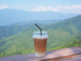 take away glass of capuccino coffee over green mountain background.