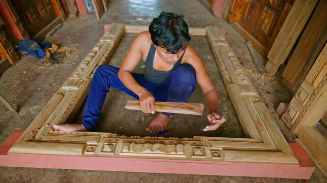 Artisan sits shaping timber board with mallet and chisel