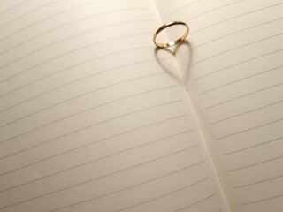 Shadow of love symbol from gold ring on blank pages of open notebook
