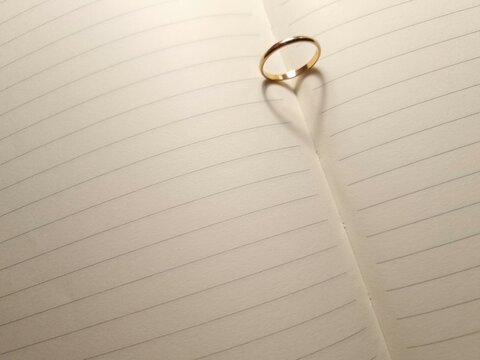 Shadow of love symbol from gold ring on blank pages of open notebook
