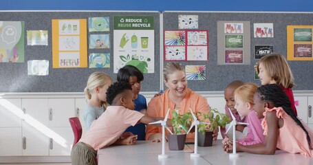 In school, female teacher and students discussing wind turbines and plants in classroom - Powered by Adobe