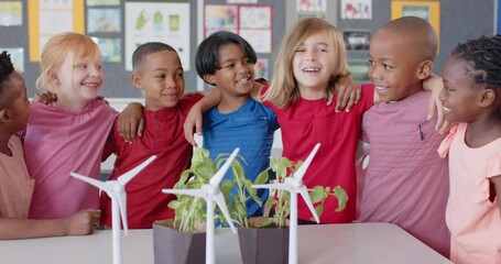 In school, diverse group of children smiling and hugging near wind turbines - Powered by Adobe