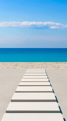 Obraz premium Bright white walkway leading to a serene beach with turquoise waters on a sunny day