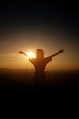Silhouette of woman open arms on top of the mountain at sunset