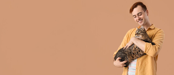 Young man with cute cat on beige background