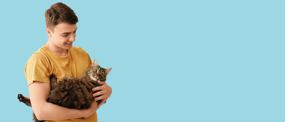 Young man holding cute cat on blue background
