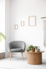 Interior of light living room with cozy grey armchair and houseplant on wooden coffee table