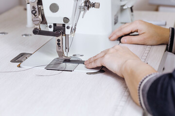Tanners hands sew black leather strips on a sewing machine indoor, selective focus.