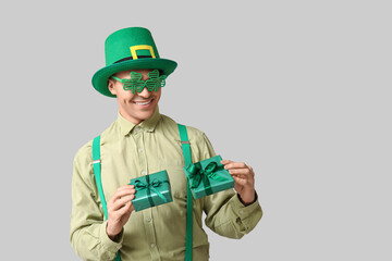 Happy young man in leprechaun's hat and with gifts on light background. St. Patrick's Day