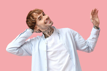 Young tattooed man dancing against pink background