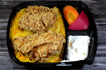 Broasted chicken meal with colorful Basmati rice, pickled slices of carrot, cucumber, turnip, fried potato chips, a broast chicken pieces, broasting combines pressure and traditional shallow frying