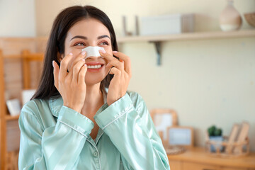 Young woman applying nose patch in bedroom