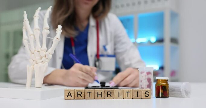 Word Arthritis of wooden cubes with human palm bones model against doctor. Swelling and tenderness of joints with painful symptoms slow motion