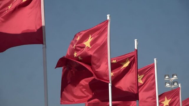 The national flags of China waves on a flagpole in the wind against the sky, representing the People's Republic of China (PRC).