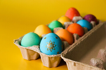 Colored Easter eggs in a cardboard box. Close-up on yellow background