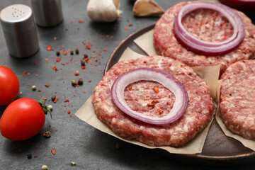 Tray with raw meat cutlets and onion on black background, closeup