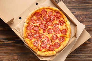 Cardboard box with delicious pizza on wooden background