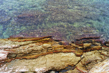 Natural background: bright layered rocks of yellow, red and pink colors and calm water. Surfaces and textures on the Adriatic coast: beautiful wild beach near Sveti Stefan, Montenegro