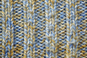 A product knitted using two different techniques from natural multi-colored yarn. Blue and yellow sweater with a combination of stockinette stitch and purl stitch close-up. Cozy background.