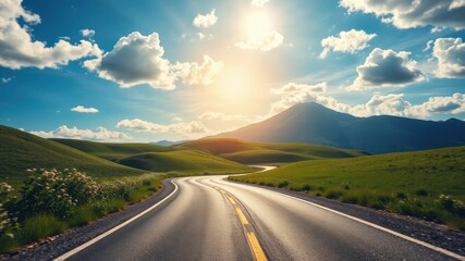 Naklejka premium A winding asphalt road leading through a picturesque landscape of rolling green hills, with a majestic mountain range in the background and a vibrant blue sky dotted with fluffy white clouds.