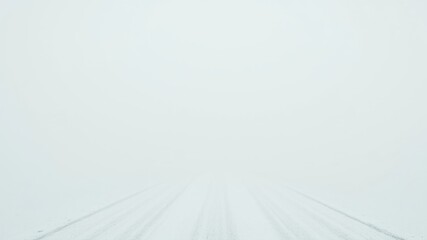 A snowy road disappears into the thick fog, creating an atmosphere of mystery and isolation.