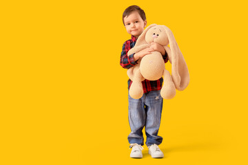 Cute little boy hugging toy bunny on yellow background