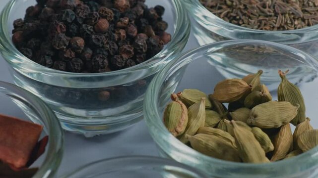 different types of whole spices Shahjeera, Kali mirch, Choti elaichi, Dalchini, Laung and Sukhi lal mirch in small glass bowl, 4k, push back shot