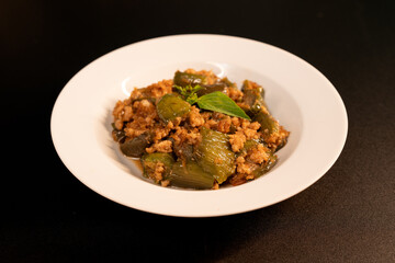 Stir-fried long eggplant (aubergine) with minced pork, on black background.
