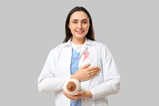 Female doctor with pink awareness ribbon and knitted breast model on light background