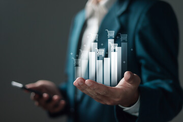 Sale growth concept. Businessman holding graph of increase in sales volume with shopping cart on virtual screen for ecommerce growth.