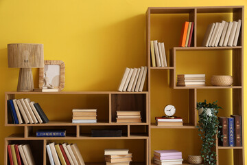 Wooden bookshelves with lamp and decor near yellow wall © Pixel-Shot