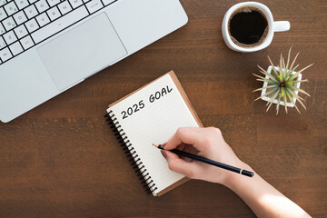Top view of hand writing 2025 goals on a notebook and coffee on wooden desk. Business goal achievement and action plan concept