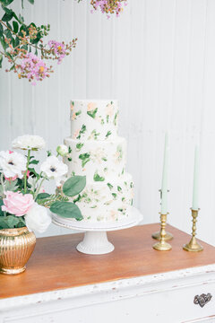 Three-tier floral cake with nearby flowers and brass candlesticks.