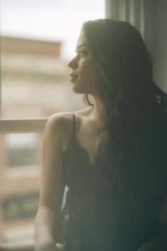 Woman in black lace gazing out window, soft focus and moody lighting