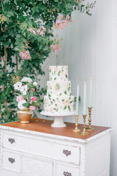 Floral wedding cake on a vintage table with pink flowers and candles.