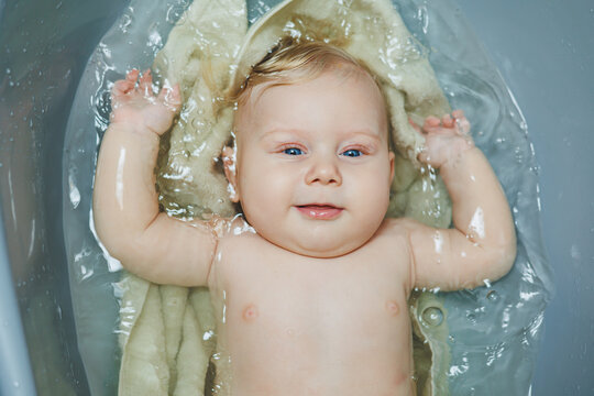 A small newborn boy of 5 months is bathing in a bathtub. Baby care.