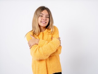 Charming pleased Beautiful caucasian teen girl wearing orange sweater embraces own body, pleasantly feels comfortable poses. Tenderness and self esteem concept
