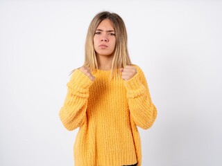 Beautiful caucasian teen girl wearing orange sweater crosses arms and points at different sides hesitates between two items or variants. Needs help with decision