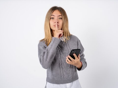 Beautiful teen girl wearing grey sweater holding modern gadget ask not tell secrets