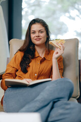Obraz premium Young woman enjoying a healthy sandwich while reading a book in a cozy indoor setting, emphasizing relaxation and comfort with a warm color palette