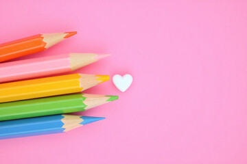 Colorful pencils arranged with heart shaped eraser on pink