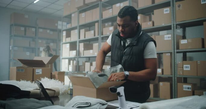 African American Warehouse Clerk, Postal Worker Packs Cardboard Box with Online Order, Prepares Parcel for Shipping to Customer, Uses Tablet Computer. E-Commerce Store Sorting Center, Delivery Service