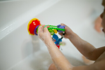 Children kid bath tube time colorful toys with suction and children arms playing in bath washing foams