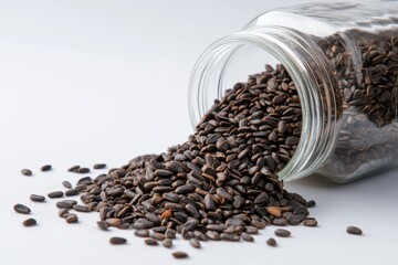 Black seeds spilling from a clear glass jar onto a white surface, showcasing their glossy texture and natural color in a rustic and appealing composition
