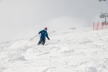Action photo of a male skier in blue outfit on a slope going down a mountain in the Alps. Active winter recreation, going down a mountain on a cloudy day. © yanik88