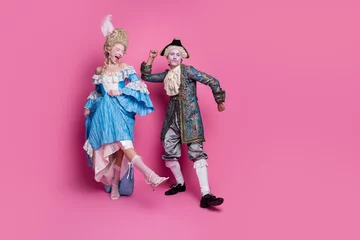 A lively couple dressed in elegant baroque costumes on a vivid pink background, showcasing the joy