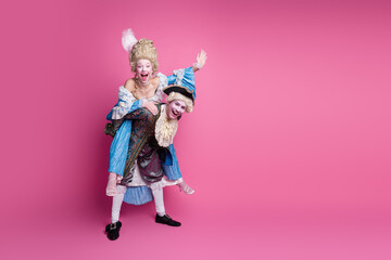 Elegant couple in baroque costumes enjoying playful moment against vibrant pink backdrop at themed carnival party
