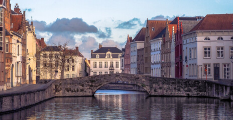 Naklejka premium Beautiful old European houses line the canal in Bruges, Belgium where an arched bridge crosses the river.