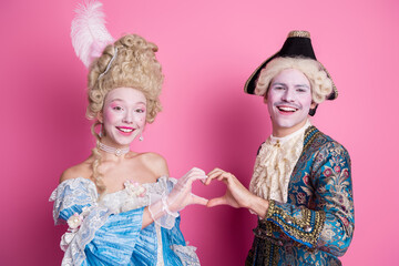 Elegant couple in classic baroque costumes posing against pink backdrop, showcasing vibrant historical fashion